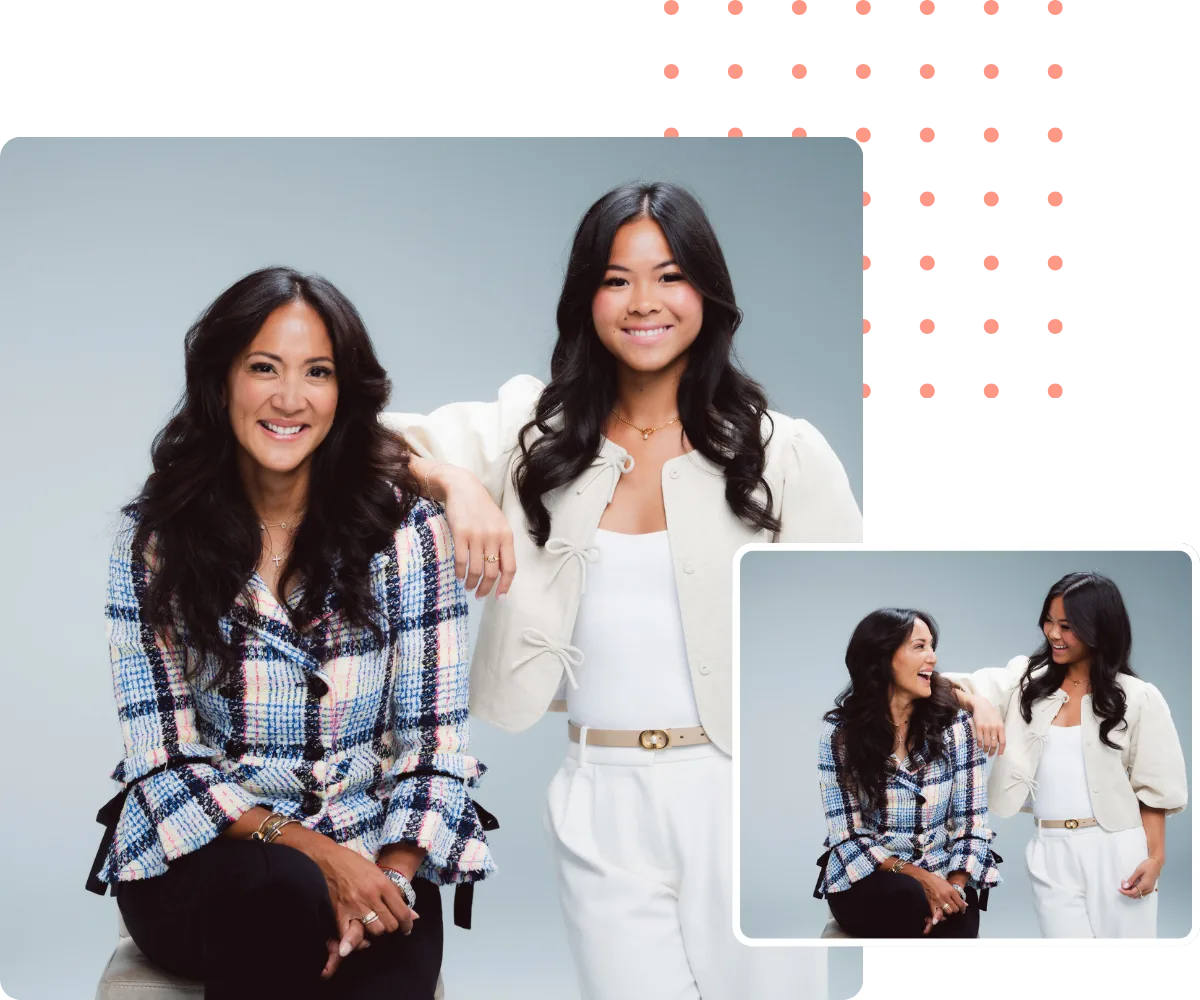 Two women smiling, posing for a portrait. One sits, wearing a blue patterned jacket. The other stands, in a cream jacket.